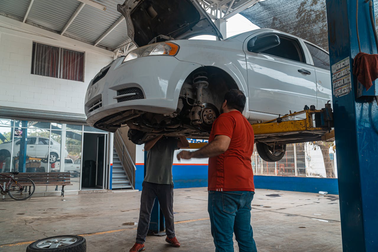 services-05 Two mechanics inspecting a white car on a lift inside a garage workshop.