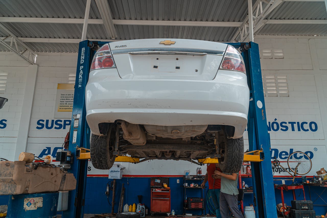 services-06 A white Chevrolet car is lifted for maintenance in an automotive repair shop.