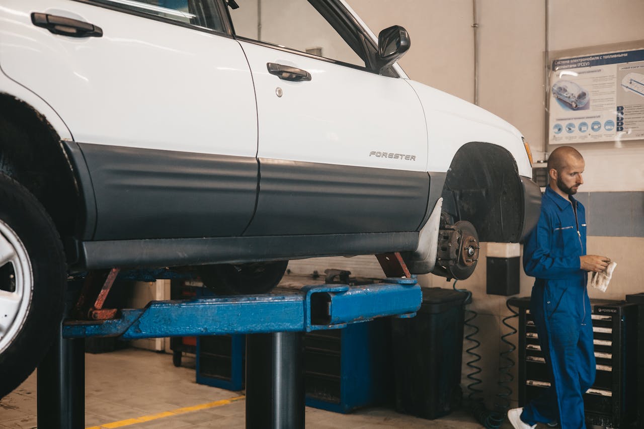 why-choose-us Mechanic evaluating a car on a lift for maintenance in an auto workshop.